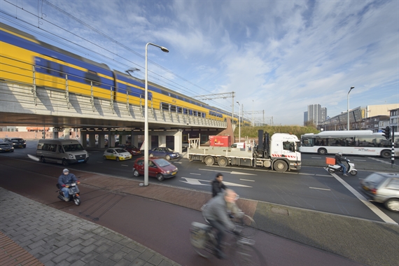 vrachtwagens, auto's en fietsers rijden onder een treinviaduct